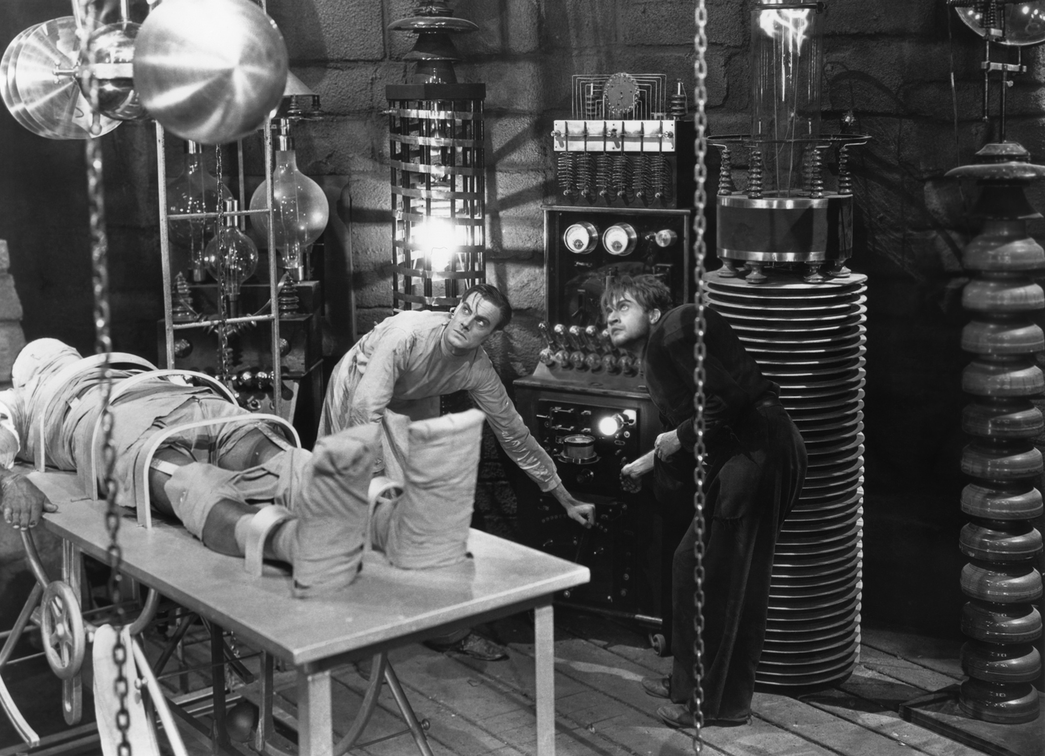 Two figures operate spooky machinery, referencing the Frankenstein &ldquo;lighning charges the body&rdquo; scene
